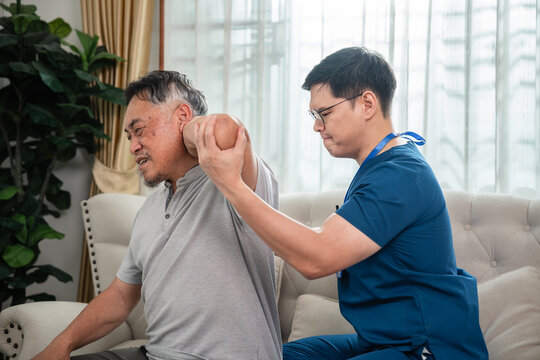 Senior Physical Therapy with a Male Caregiver Assisting Shoulder Mobility for an Asian Elderly Man during a Home Rehabilitation Exercise in a Living Room