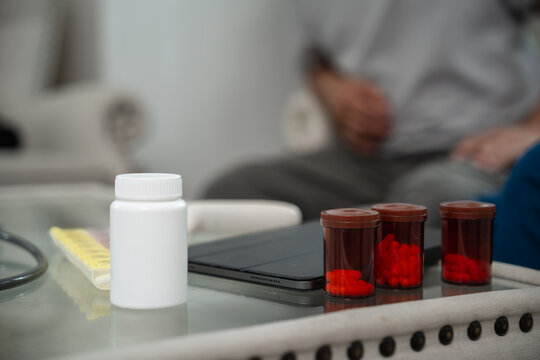 Senior Medication Management with Medicine Bottles, Pill Organizer and Digital Tablet Arranged near an Asian Elderly Man during Home Care in a Living Room