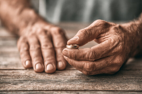 A pair of hands on a wooden table; one hand is removing a wedding ring, concept for couple problems.