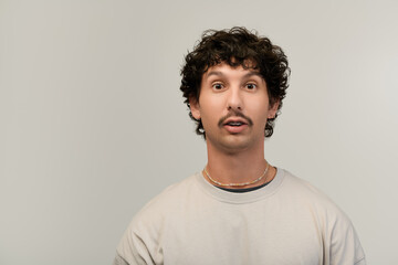 Obraz premium Young man with a playful smile and stylish moustache poses against a neutral backdrop