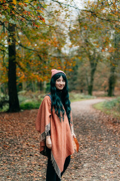 Young Woman wrapped in warm Shawl Poncho enjoying autumn walk in forest with fall yellow leaves. Travel lifestyle. Feeling harmony, reunion with nature. Relaxing, personal fulfillment. Local travel.