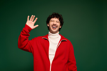 Fototapeta premium Young man with moustache joyfully greeting in stylish red outfit against green backdrop