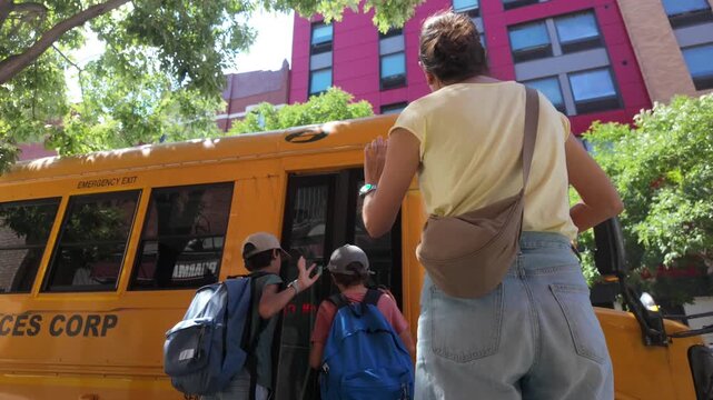 Mother waving goodbye to her sons boarding the yellow school bus for their first day of school, a heartwarming family moment showing parental love and the daily education routine