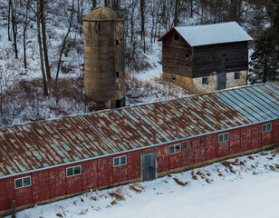 Rural Winter Farmstead with Red Barn, Concrete Silo, and Weathered Wooden Barn Surrounded by Snow and Leafless Trees © Jason