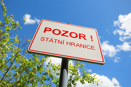 Czech green border warning sign with text Pozor! St&aacute;tn&iacute; hranice (translation: Attention! State Border). Sunny with clear blue sky and green vegetation. Copy space, shallow focus, low angle view.