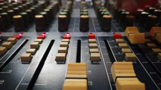 Macro shot of a music producer hand adjusting volume faders on a professional sound mixing desk