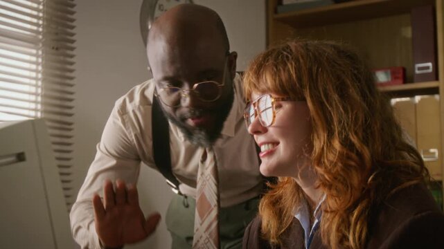 Caucasian woman and African American man looking at vintage computer monitor, celebrating success in retro office. Video is ideal for retro business marketing