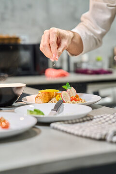 Chef sprinkling seasoning on gourmet salmon plate