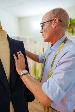 Mature tailor adjusting custom blazer on mannequin, creating bespoke fashion in his professional workshop