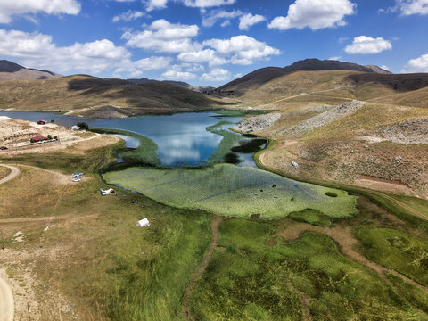 Aerial view of Egri Gol surrounded by rolling hills, lush green wetlands, and blue water under a bright sky in Akseki, Antalya, Turkiye.