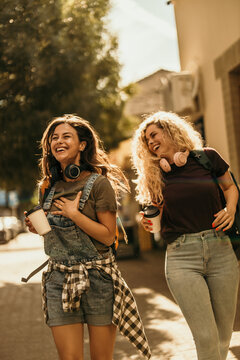 Young women friends laughing walking street enjoying coffee