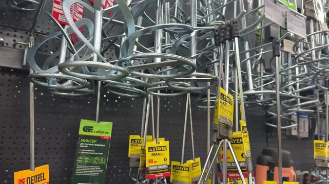 Barnaul, Russia, 15 July 2026 - Hardware store display of galvanized metal mixer attachments and paddle stirrers for drills hanging on pegboard wall.