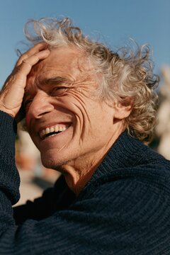 Laughing man with gray hair and deep wrinkles in navy sweater for outdoor poster background and candid lifestyle design
