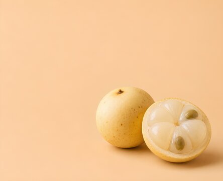 Exotic Fruit Still Life - Langsat (Lanzones). Fresh Langsat  cut in half revealing juicy flesh and seeds, placed on a soft peach background for a clean and minimalist presentation