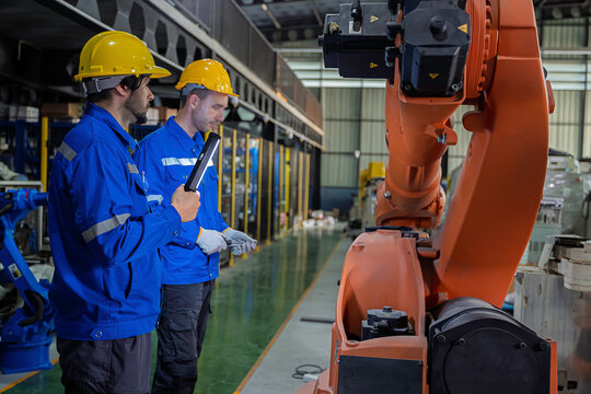Two industrial engineers inspect a robotic arm during maintenance in a smart manufacturing facility, highlighting automation, engineering, teamwork, industrial robotics