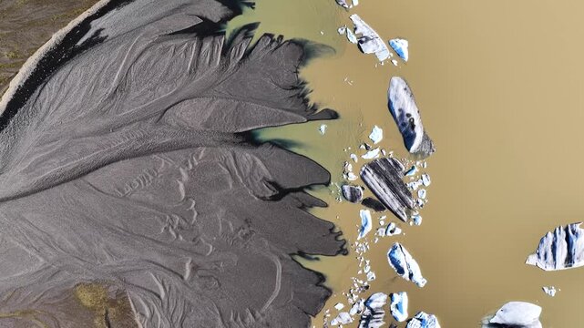 Aerial view of a glacial river delta with dark volcanic sand patterns and floating icebergs in the lagoon near Hofn, Sveitarfelagid Hornaf, Iceland.
