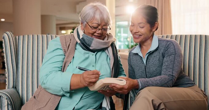 Writing, book and nurse with old woman on sofa for crossword puzzle, support or help in living room. Alzheimer prevention, strategy game and trivia solution with people in home for answer and bonding