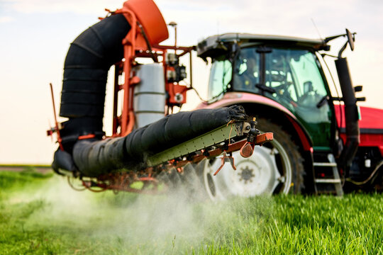 Tractor spraying pesticide on green wheat field, contributing to modern agriculture