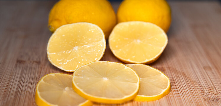 Close-up of two lemons on a cutting board, with sliced lemon slices in the foreground. Subtropical fruit, contains vitamin C, freshness, citrus fruit, healthy eating.