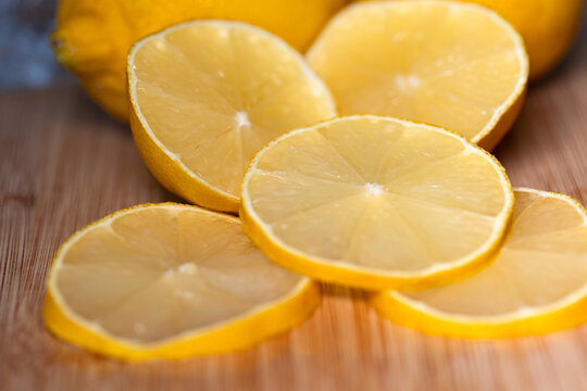 Close-up of two lemons on a cutting board, with sliced lemon slices in the foreground. Subtropical fruit, contains vitamin C, freshness, citrus fruit, healthy eating.