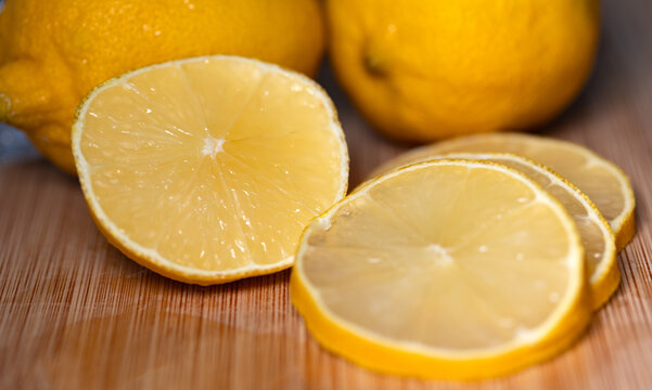 Close-up of two lemons on a cutting board, with sliced lemon slices in the foreground. Subtropical fruit, contains vitamin C, freshness, citrus fruit, healthy eating.