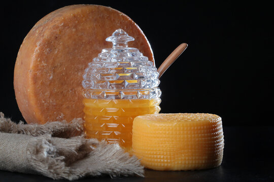 Two types of cheese and honey on dark background. Still life with large diameter and smaller cheese head. Honey is poured in glass honey pan