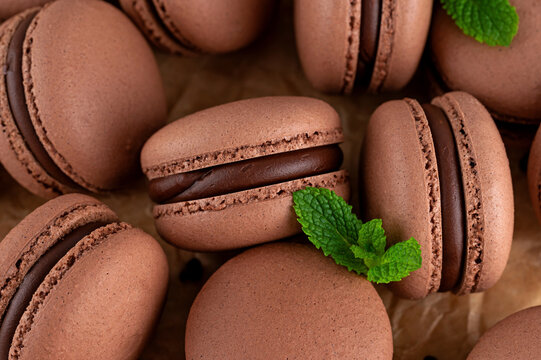 Dark chocolate macarons with chocolate ganache filling and mint on parchment paper. Sweet french meringue cookies macaron. Top view, close up.