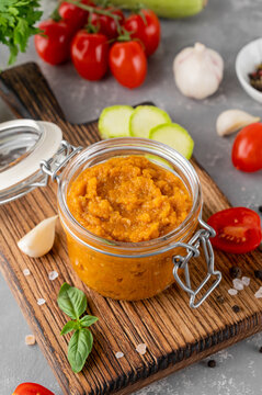 Zucchini caviar in a glass jar with fresh vegetables and herbs on a rustic board, homemade vegetable spread for healthy eating and canning. Copy space.