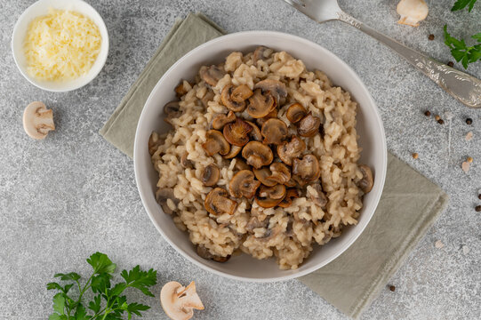 A creamy mushroom risotto topped with parmesan and herbs, served in a white bowl on a gray concrete background. Top view, copy space.