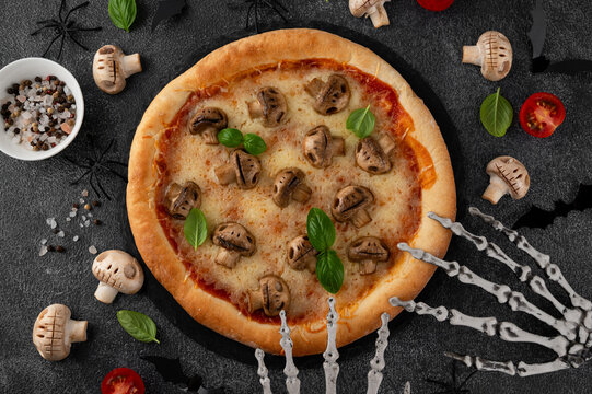 Halloween mushroom pizza with basil, cheese and spooky skeleton decoration on a dark background, creative food concept for seasonal menus. Funny food idea. Top view.
