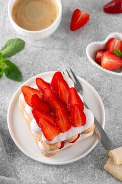 Strawberry tiramisu. Italian layered dessert with mascarpone cream and biscuits on a plate with cup of coffee on a concrete background.