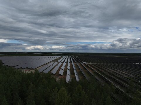 Aerial view of a large solar park with rows of photovoltaic panels extending across the landscape near a forest under a cloudy sky in Utajarvi, North Ostrobothnia, Finland.