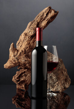 Glass and bottle of red wine with old wooden snag and a piece of granite rock.