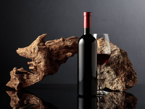 Glass and bottle of red wine with old wooden snag and a piece of granite rock.