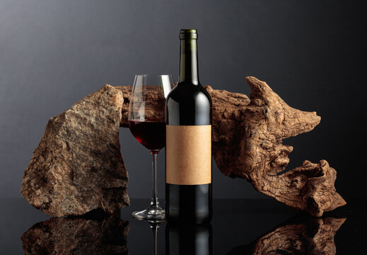 Red wine with old driftwood and a piece of granite rock on a black reflective background.