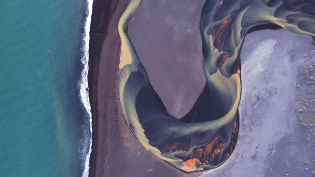 Aerial view of a braided river delta with intricate channels of glacial sediment flowing into the dark blue ocean along the black sand coastline of Iceland.