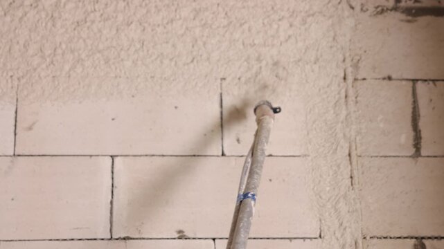 cement plaster, Fresh mortar, Wall insulation. Tight view hose nozzle applying fresh plaster finish to inside block wall in renovation project.