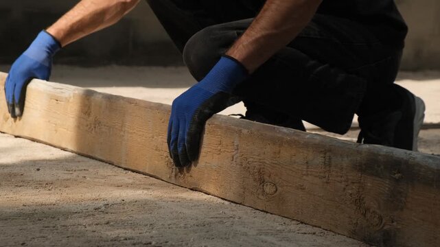 Road construction worker uses a long screed board to level the final sand base before paving stone installation at sunset. Seasonal road work, overtime and municipal infrastructure.