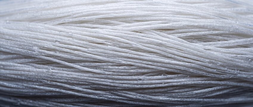 Abstract background of thin translucent white glass noodle strands bundled together creating layered texture and light effect.