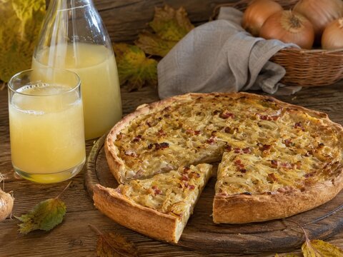 Knuspriger Zwiebelkuchen mit Federwei&szlig;er auf rustikalem Holztisch. Klassische deutsche Herbstspezialit&auml;t zur Weinlese mit regionaler Tradition und saisonalem Genuss.