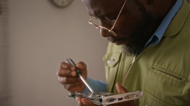 African American man using screwdriver to repair computer graphics card, camera tilting up. Footage is perfect for IT support, hardware repair services, and technology education