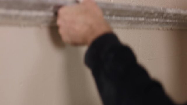 Hands closeup, Worker hands, Hand tool. Close-up wall finishing with straightedge used to flatten wet plaster on interior surface.