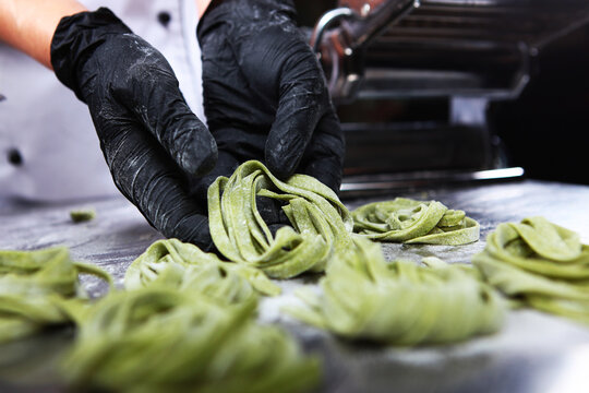 Cook's hands in black gloves form nests of fresh homemade spinach paste on floured metal countertop