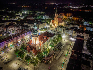 Nocna panorama rynku w Oławie z dronu. Podświetlony ratusz, kościół i zabytkowe kamienice dolnośląskiego miasta. Przestrzeń miejska, architektura i turystyka regionalna w Polsce. © Henryk Niestrój