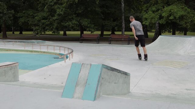 A mature man jumping onto an obstacle and sliding down on aggressive inline skates at an outdoor skatepark