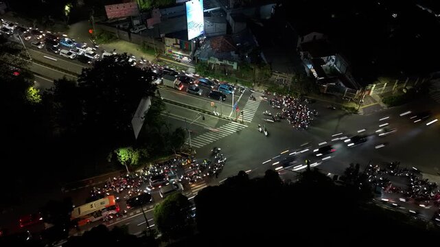 Aerial view of Jalan Panjang intersection at night with light trails from moving traffic in Kecamatan Kebon Jeruk, Daerah Khusus Ibukota, Indonesia.