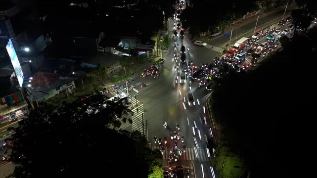 Aerial view of Jalan Panjang intersection at night with light trails from heavy traffic and city skyline in the background in Kecamatan Kebon Jeruk, Daerah Khusus Ibukota, Indonesia.