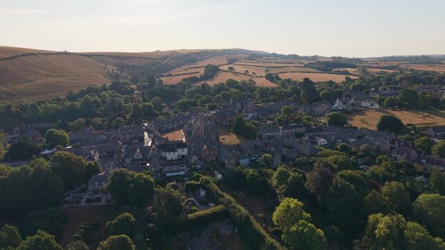 Aerial drone footage of Corfe village in Dorset, England, featuring traditional stone cottages, rolling countryside, green fields, and the scenic Purbeck landscape on a bright summer morning