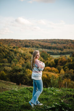 Girl in the mountains. Woman standing on a hill with arms crossed, overlooking an autumn forest. Female enjoying the view in nature on a windy day.