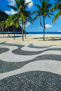 Famous Copacabana beach promenade in Rio de Janeiro with its iconic wave mosaic pavement, tropical palm trees, and sunny blue sky.